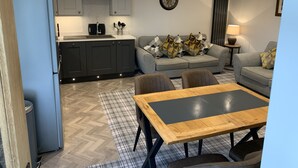 A modern living room with a grey sofa, a wooden coffee table, and a kitchen area with grey cabinets and a built-in oven. - Newly converted barn with hot tub,stylish interior and outdoor space (Roundthwaite)