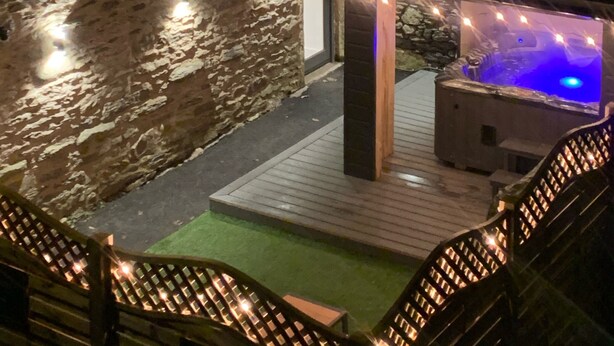 A stone wall, a wooden deck, and a hot tub with lights. - Newly converted barn with hot tub,stylish interior and outdoor space (Roundthwaite)