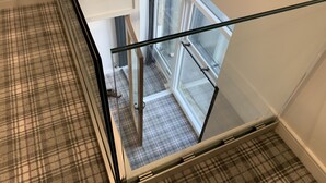 A view from a window on the second floor of a building, looking down at a staircase with a plaid carpet. - Newly converted barn with hot tub,stylish interior and outdoor space (Roundthwaite)