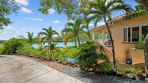 Una casa con piscina, rodeada de vegetación tropical y una vista despejada al mar.