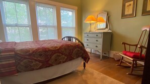 A bedroom with a bed, dresser, rocking chair, and a lamp.