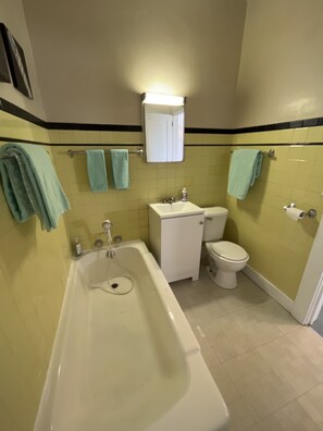 Un baño con bañera, inodoro y lavamanos. Hay toallas colgadas en un perchero.