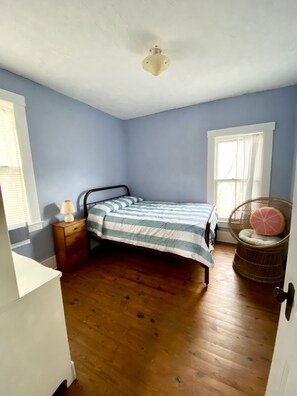 Un dormitorio con una cama, una mesita de noche, una silla y una ventana.
