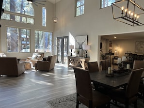 Un vaste salon doté d’un haut plafond, de grandes fenêtres et d’un coin repas avec une table et des chaises en bois.