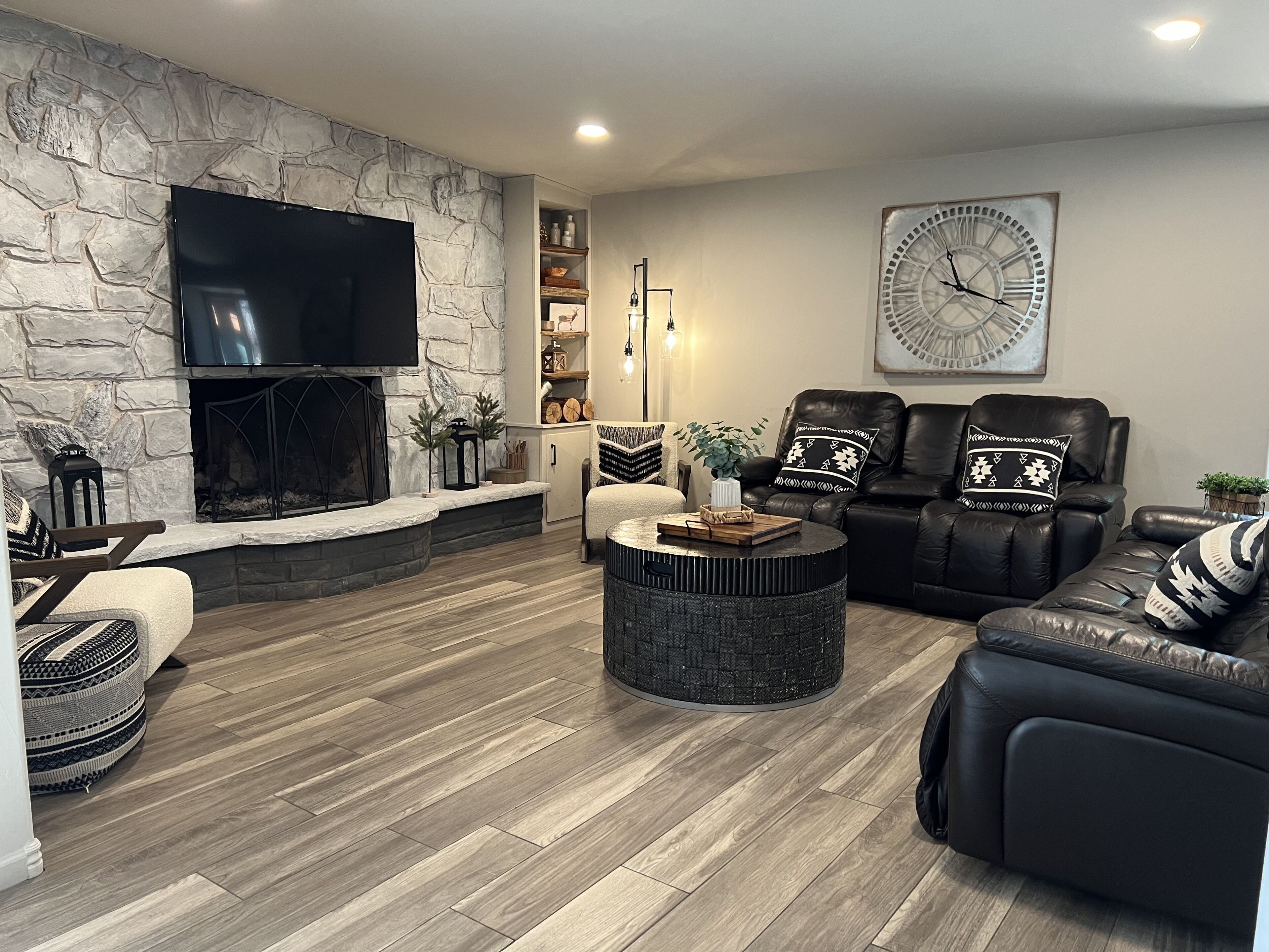 A living room with a stone wall, fireplace, leather sofas, a round coffee table, and a large clock on the wall.