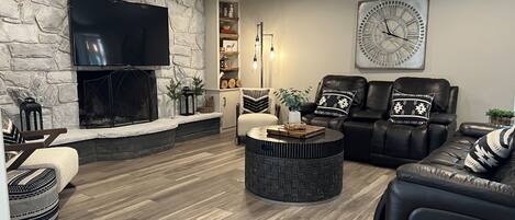 A living room with a stone wall, fireplace, leather sofas, a round coffee table, and a large clock on the wall.