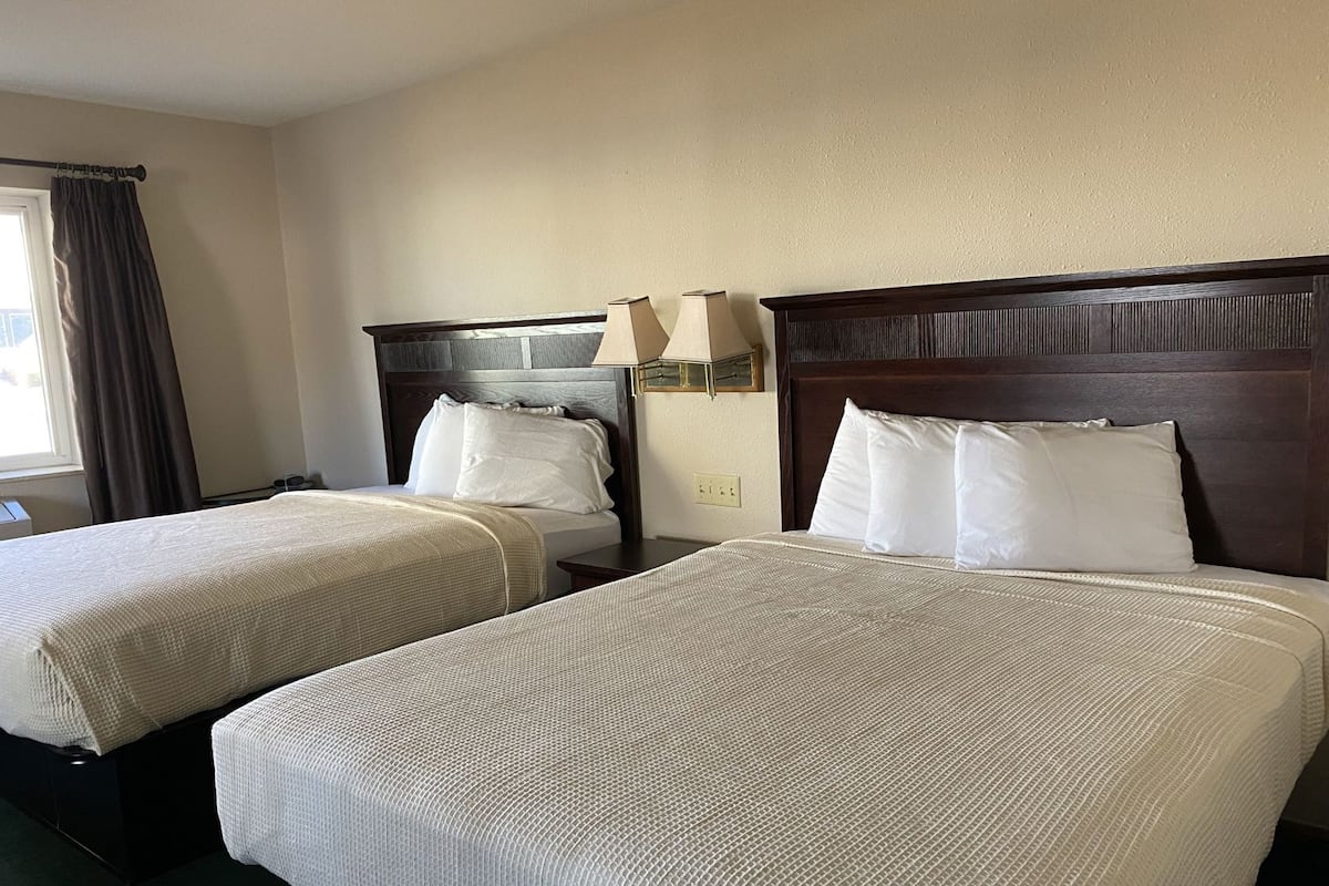 A hotel room with two beds, a nightstand with a lamp, and a window with curtains.