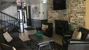 A lobby with a staircase, a fireplace, and a television mounted on the wall. - Heritage inn (Watertown)