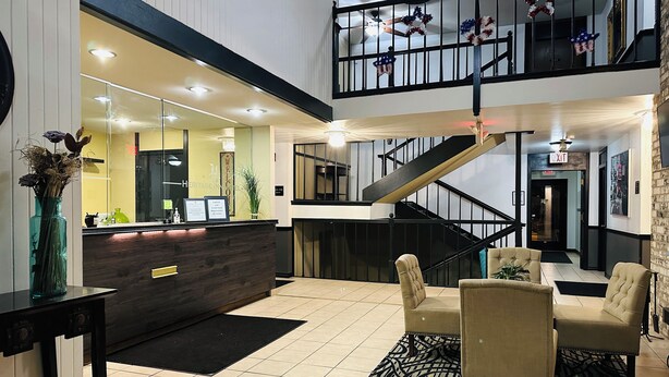 A hotel lobby with a reception desk, a staircase, and seating area. - Heritage inn (Watertown)
