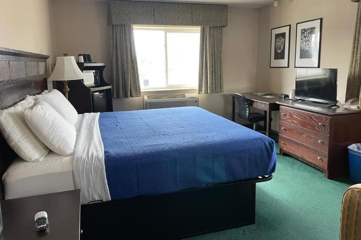 A hotel room with a bed, a desk, a television, and a dresser.