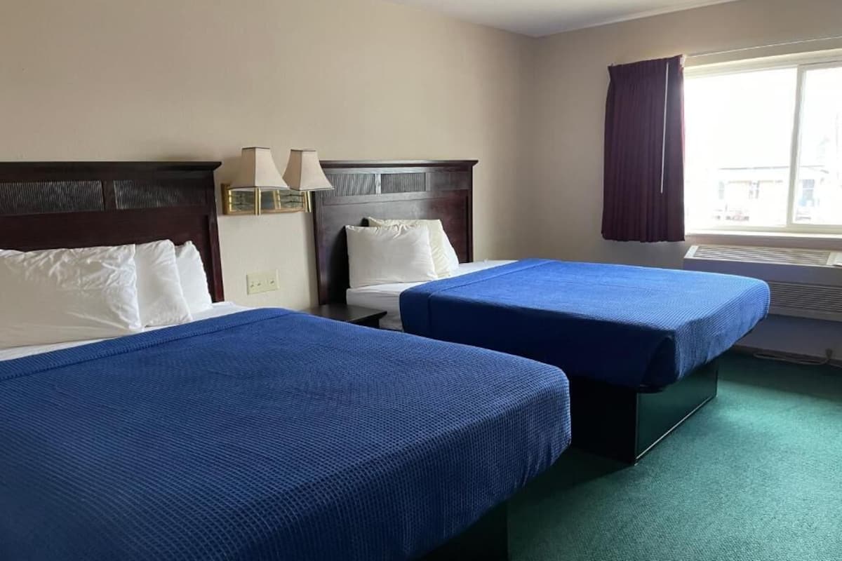 A hotel room with two beds, each with a blue bedspread, a wooden headboard, and a nightstand with a lamp.