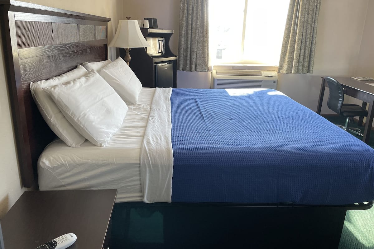 A hotel room with a bed, a desk, a lamp, and a window with curtains.