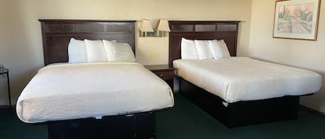 Habitación de hotel con dos camas individuales, una mesita de noche con lámpara, un cuadro en la pared y una alfombra verde.
