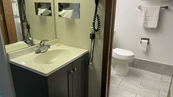 Un baño con lavamanos, espejo, secador de pelo y retrete.
