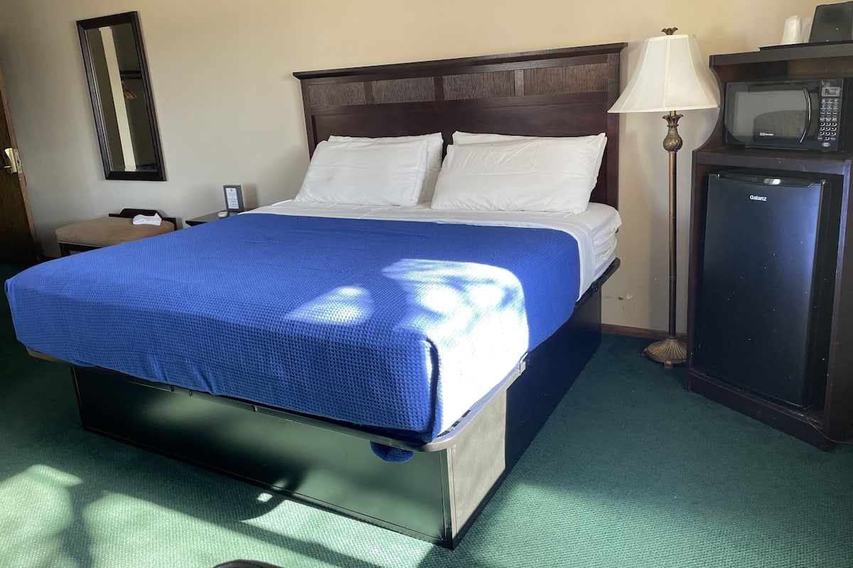 A hotel room with a bed, a nightstand, a lamp, a microwave, and a small refrigerator.