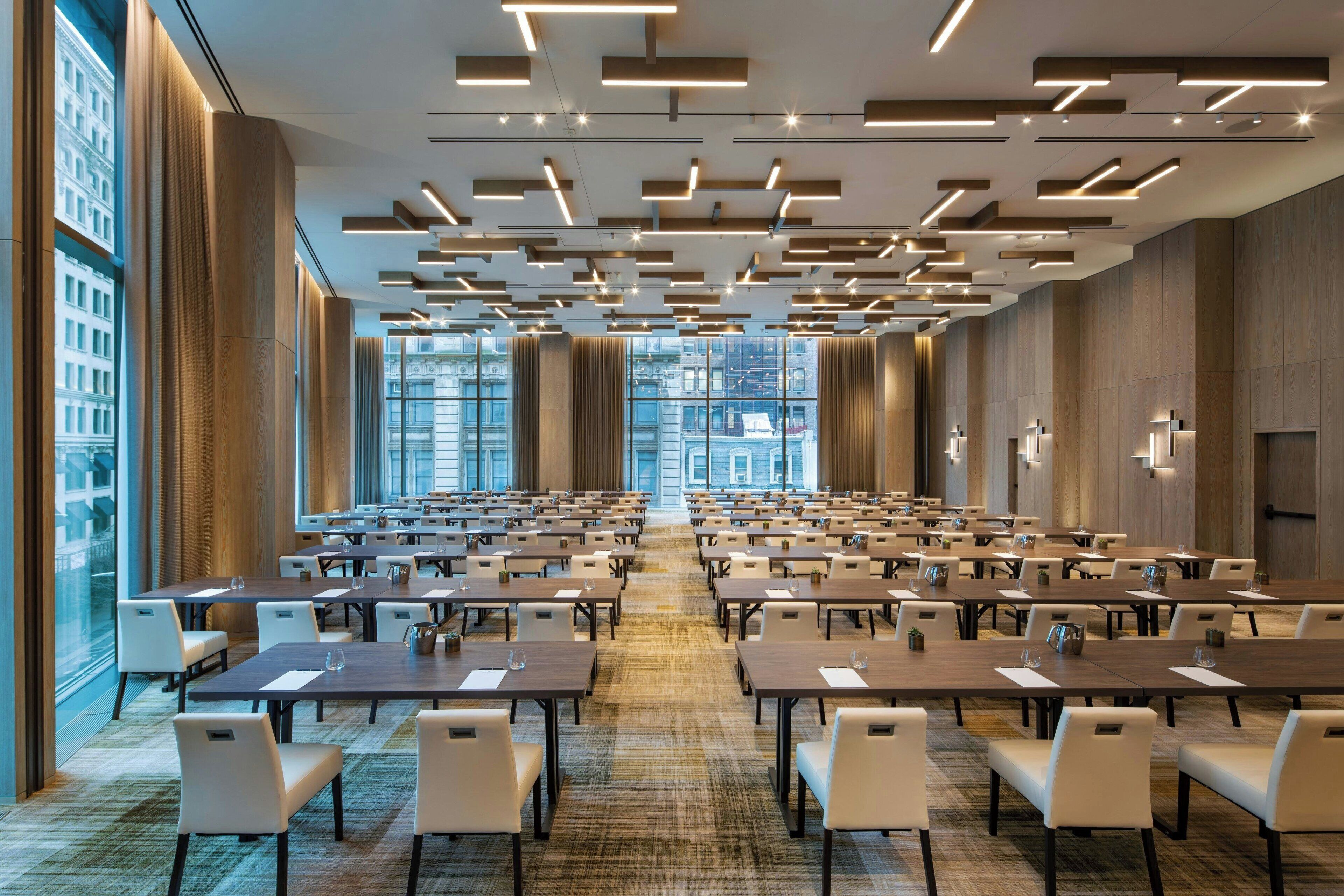 Une salle de conférence avec des rangées de tables et de chaises, de grandes fenêtres et des luminaires modernes.