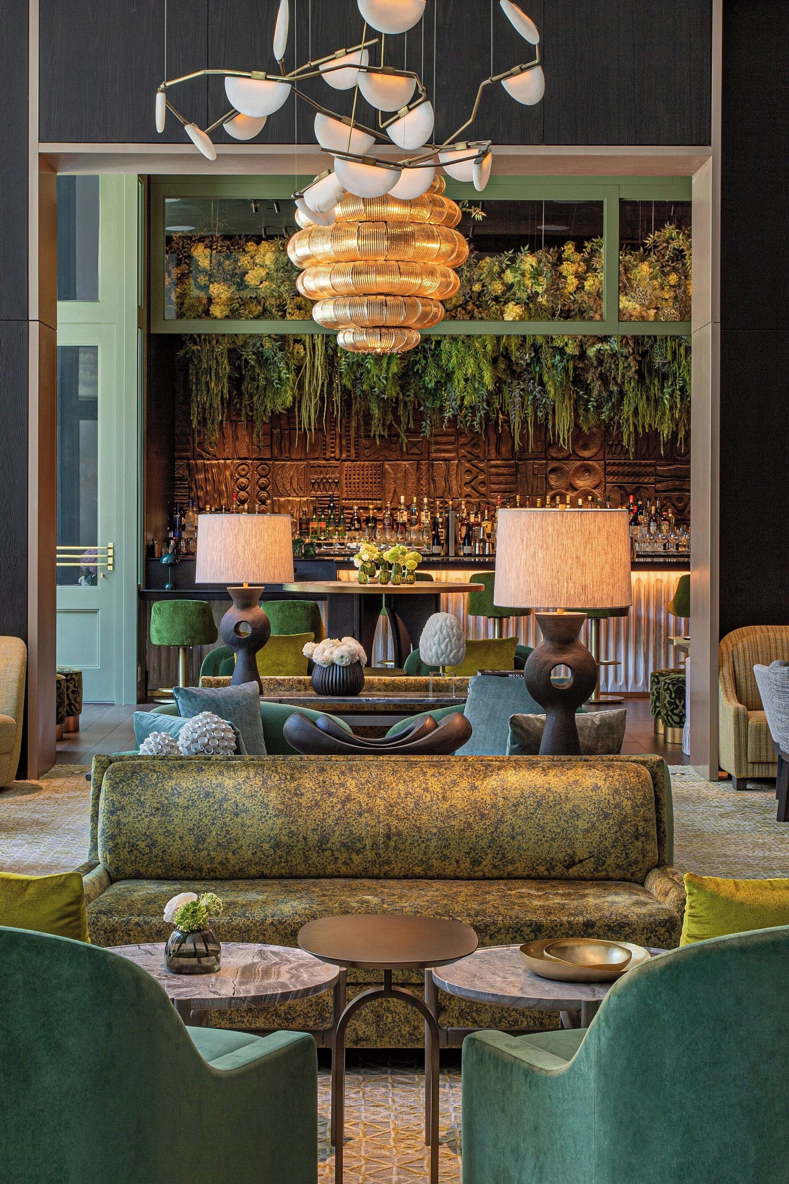 Een moderne lounge met een bank, stoelen, een bar en een decoratieve hanglamp.