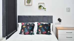 A neatly made bed with floral pillows, a bedside table with a lamp, and a small plant on the wall. - Townhouse @ 202 Walthall Street Crewe (Crewe)
