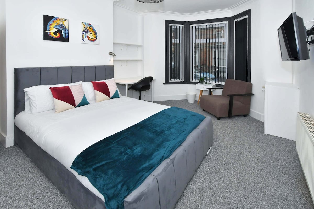 Een netjes ingerichte hotelkamer met een groot bed, een bureau, een stoel en een aan de muur bevestigde televisie.