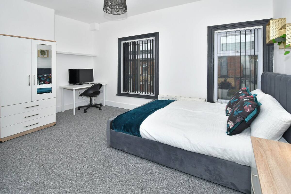 Een slaapkamer met een bed, een bureau, een televisie en een kledingkast.