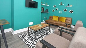 A teal-walled living room with a brown sofa, a coffee table, and a TV mounted on the wall. - Townhouse @ 202 Walthall Street Crewe (Crewe)