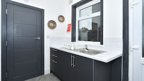 A modern kitchen with dark cabinetry, a white countertop, and a window above the sink. - Townhouse @ 202 Walthall Street Crewe (Crewe)