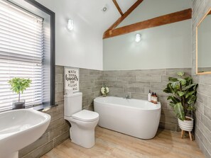 Ein modernes Badezimmer mit Toilette, Bidet und Badewanne, Holzträgern, grauen Fliesen und Topfpflanzen.