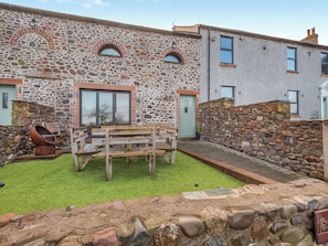 Ein Steinhaus mit einer Terrasse, einer Holzbank und einer Steinmauer.