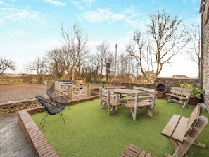 Eine Terrasse mit Holzbänken, einem schwarzen Stuhl und einer Steinmauer.