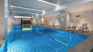 Una piscina interior con suelo de baldosas, sillas de descanso y vista despejada al área de la piscina.