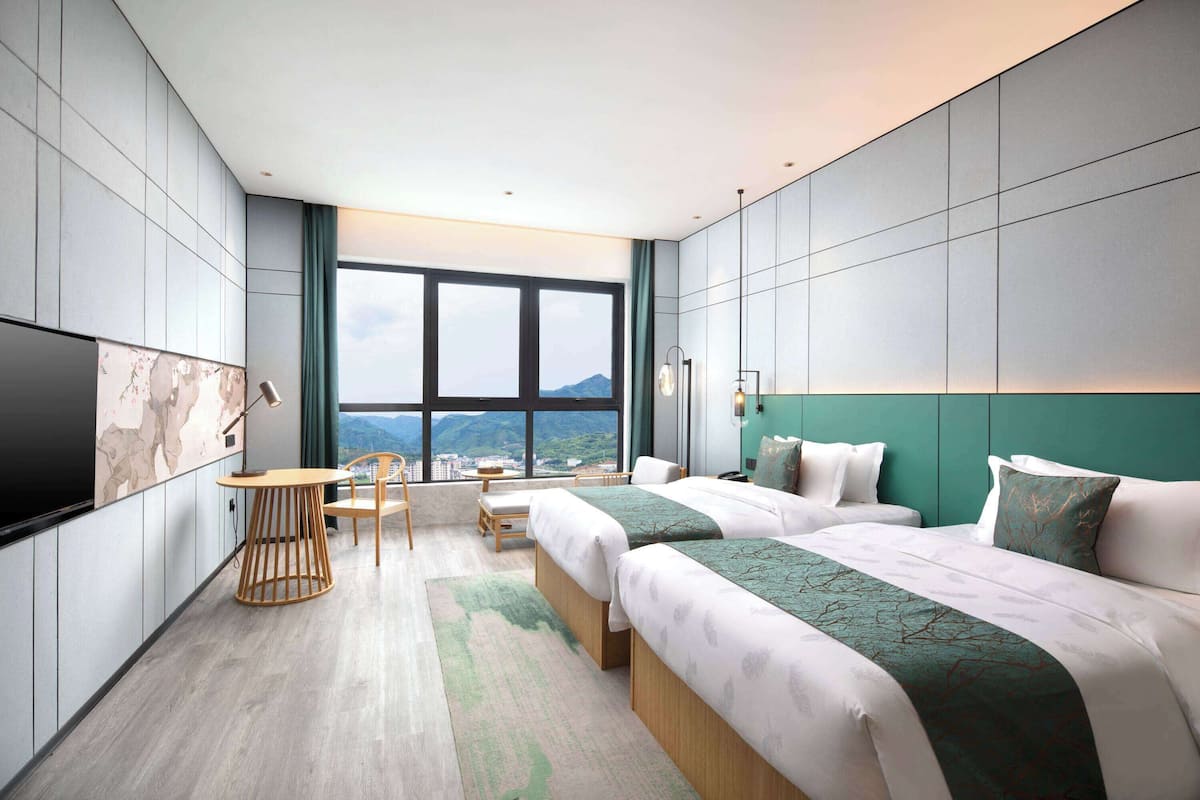 Una habitación de hotel moderna con dos camas, un escritorio y vistas a la montaña.