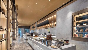 Un moderno vestíbulo de hotel con piso de mármol, una recepción y diversas comodidades, incluyendo un área de bufé con comida y bebidas.