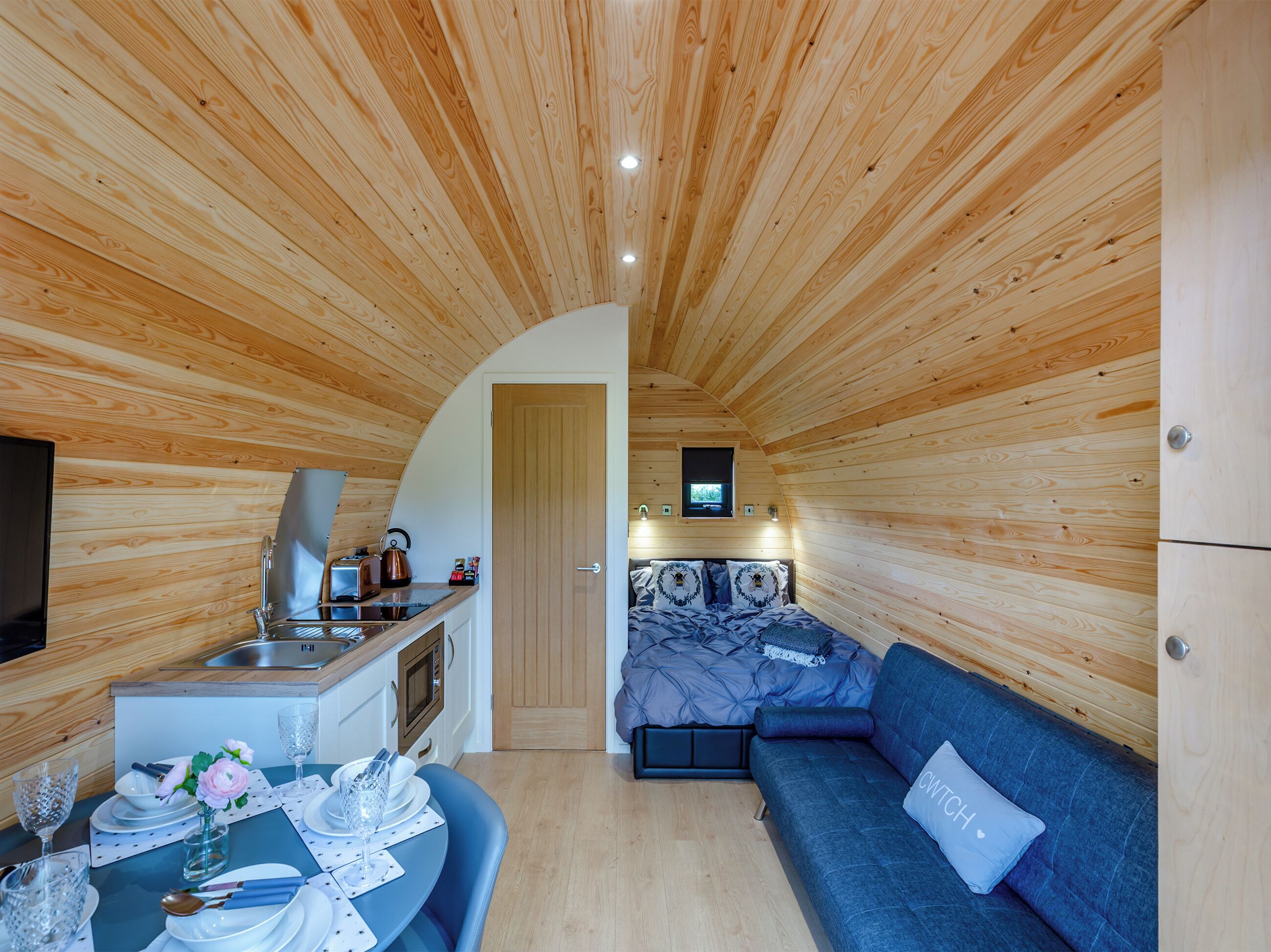 Une pièce compacte, dotée d’un plancher en bois, d’un coin cuisine, d’un espace repas et d’un canapé.