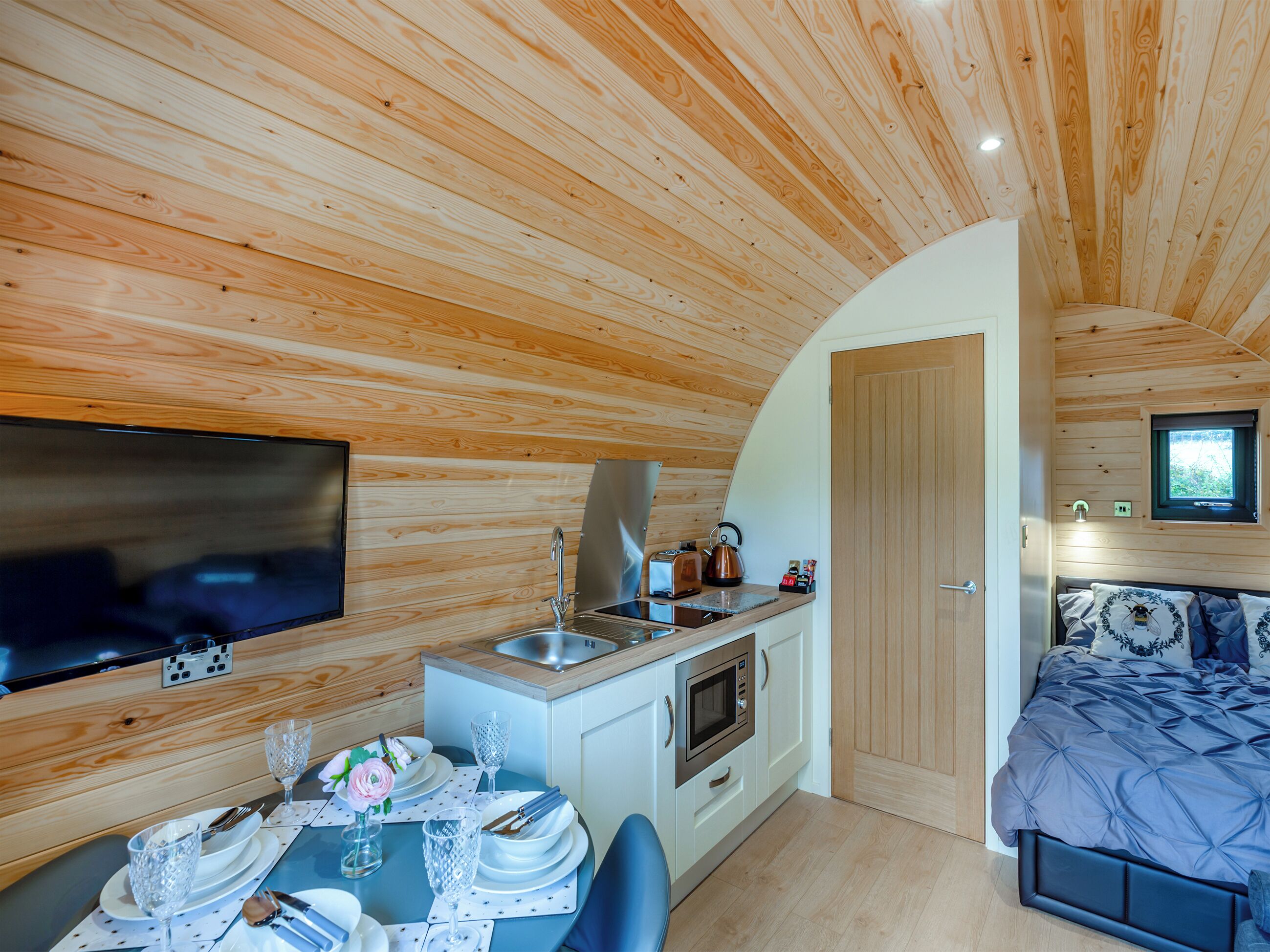 A compact, modern cabin with a wooden interior, a kitchenette, a dining area, and a bedroom.