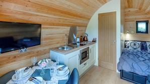 Una cabaña compacta y moderna con interior de madera, kitchenette, comedor y un dormitorio.