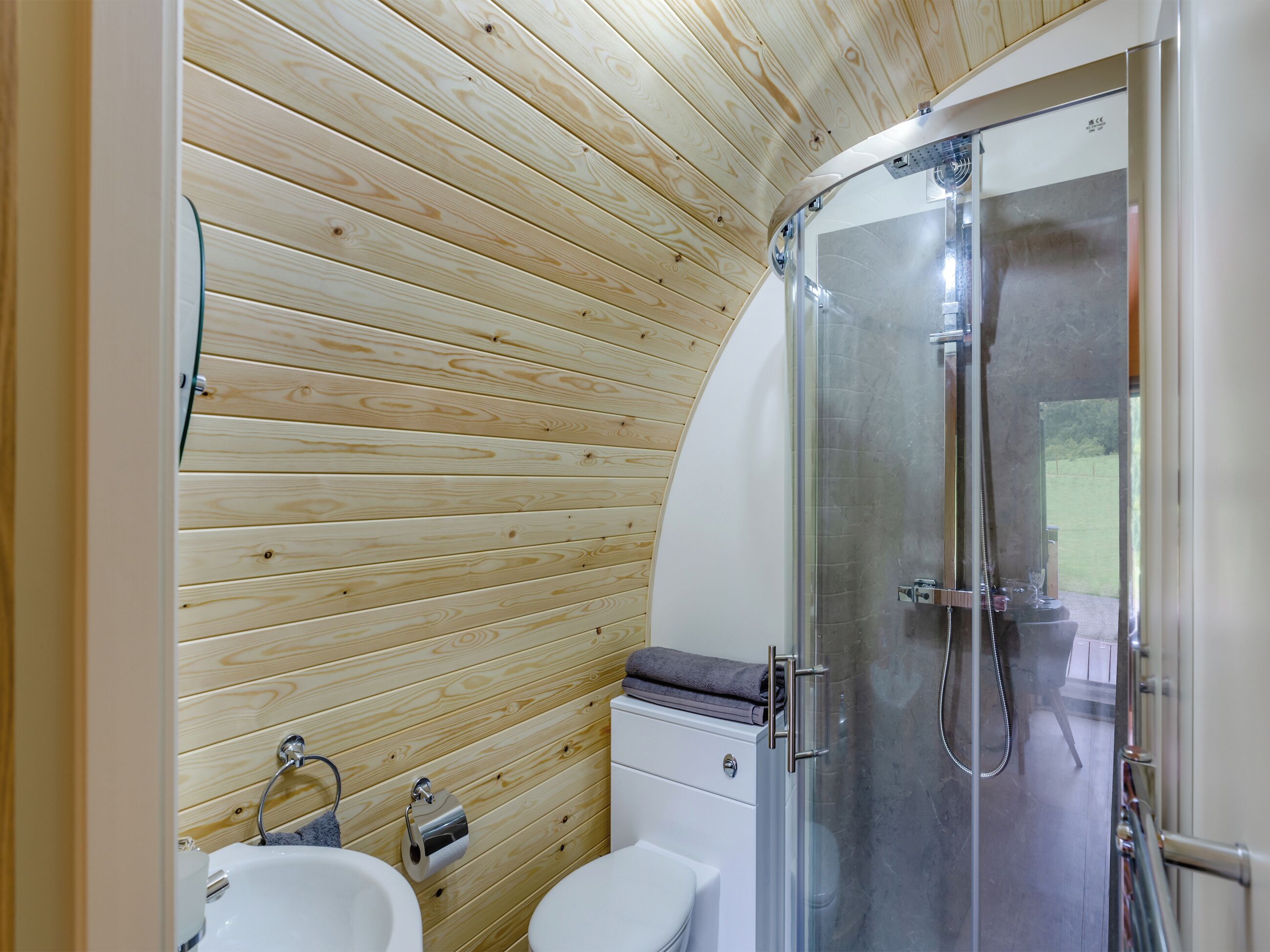 A modern bathroom with wooden panel walls, a glass shower enclosure, and a white sink.