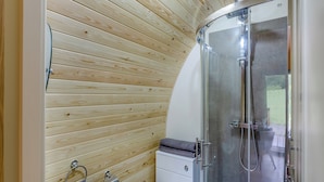 Un baño moderno con paneles de madera, cabina de ducha de vidrio y lavamanos blanco.
