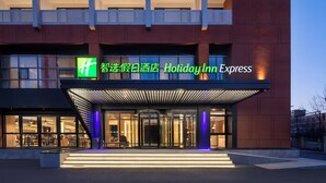 A Holiday Inn Express hotel with a modern facade, large glass windows, and a prominent entrance with a revolving door. - Holiday Inn Express Beijing Yizhuang Center by IHG (Beijing)