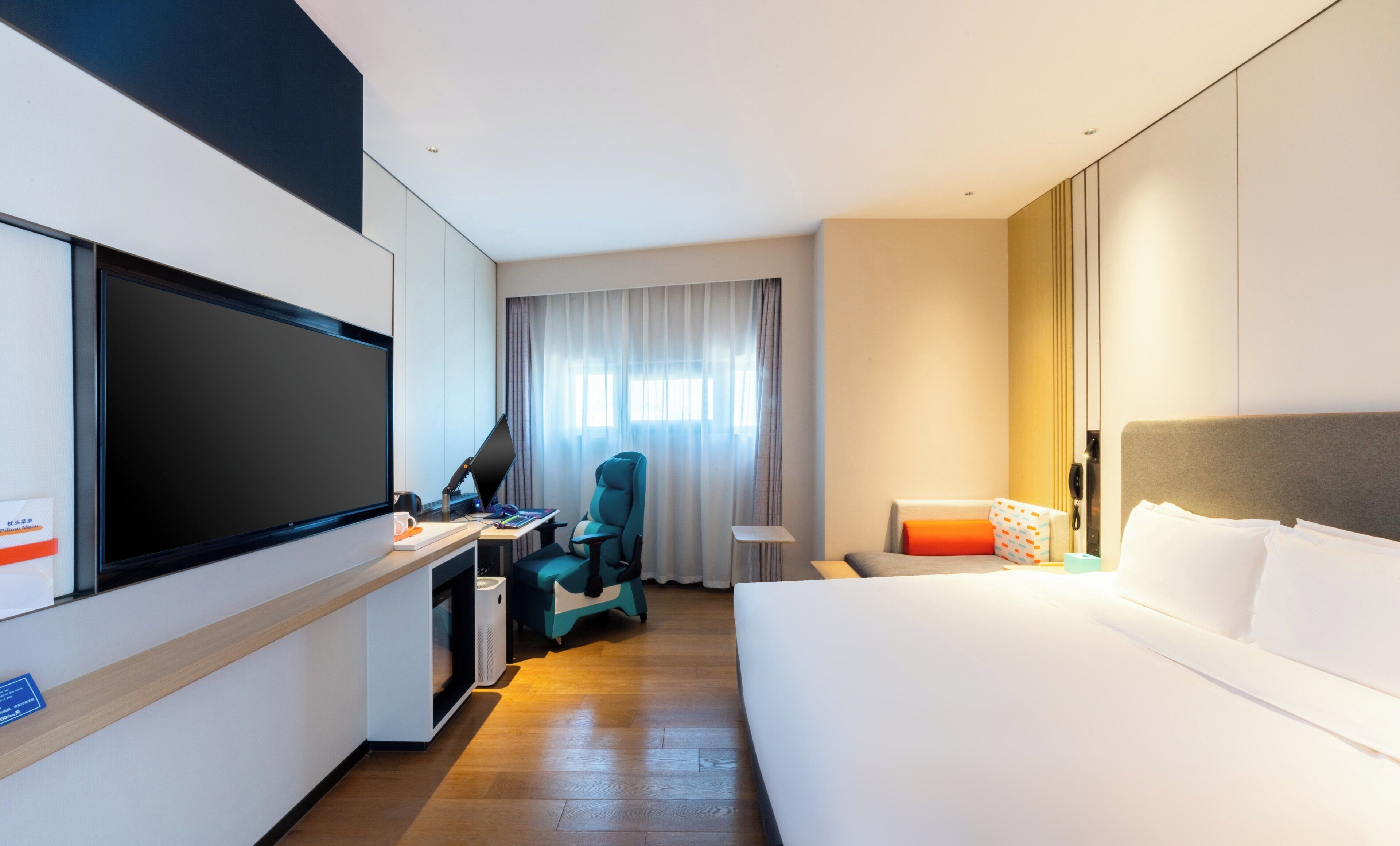 Habitación de hotel con cama, escritorio, silla, televisor y cortinas.