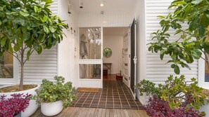 A house entrance with a wooden deck, white exterior, and potted plants.