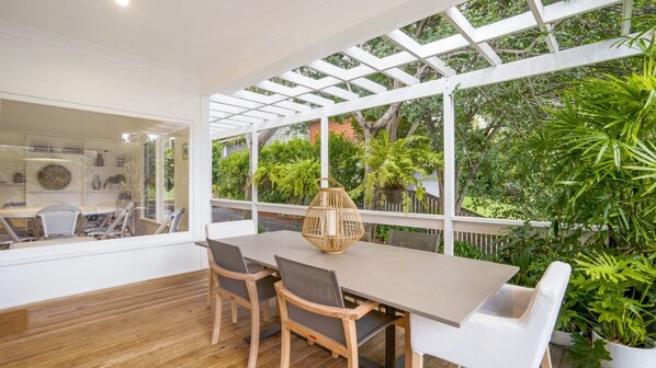 A dining area with a wooden table and chairs, a woven lantern, and a view of lush greenery through large windows.