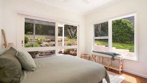 A bedroom with a large bed, a view of a garden through a window, and a wooden bench by the window.