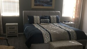 Ein Schlafzimmer mit Bett, Nachttisch, Sessel, Deckenventilator und einem Bild an der Wand.