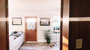 A hallway with a wooden door, a white couch, a potted plant, and a small table with items on it.
