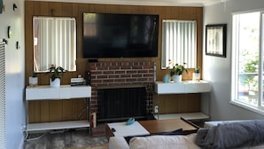 A living room with a fireplace, a flat-screen TV, a sofa, and a window with curtains.
