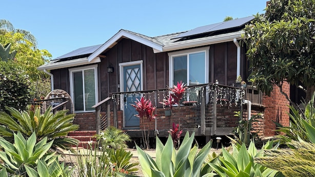 A house with a brick exterior, a front porch with a railing, and a solar panel on the roof.