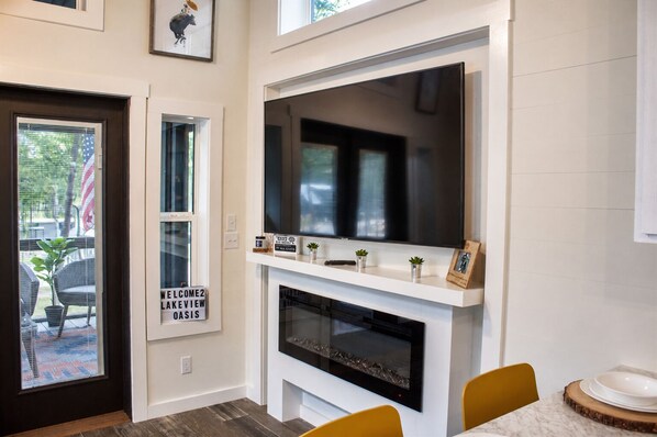 A modern interior with a fireplace, a flat-screen TV mounted above it, and a sign reading 'WELCOME TO LAKEVIEW OASIS.'