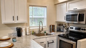 Una cocina moderna con armarios blancos, un lavamanos de acero inoxidable, un microondas y un horno.