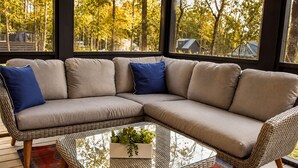 Un sofá modular con cojines azules, una mesa de centro de vidrio con una planta y una silla tejida.