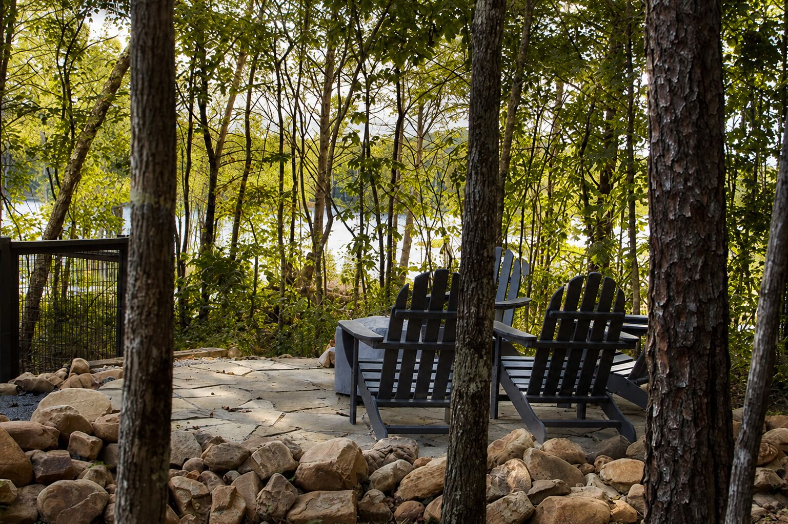 Un espacio al aire libre con sillas Adirondack y una mesa de piedra, rodeado de árboles y un paisaje rocoso.